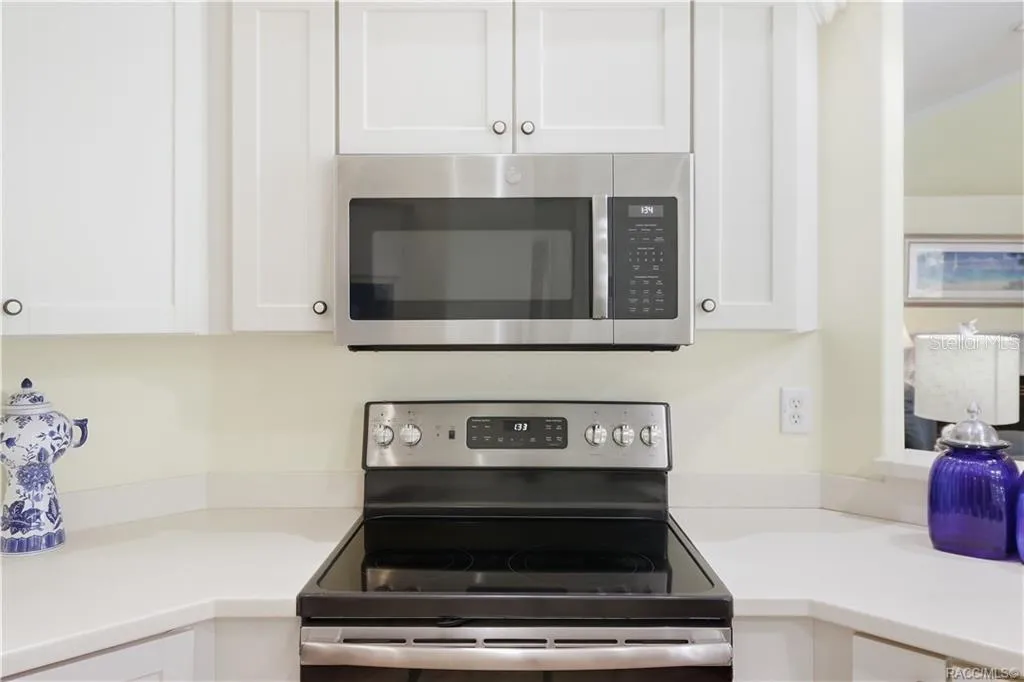 Kitchen Appliances – NEWER Stainless-steel electric range &amp; built-in microwave surrounded by white cabinetry and corian countertops.