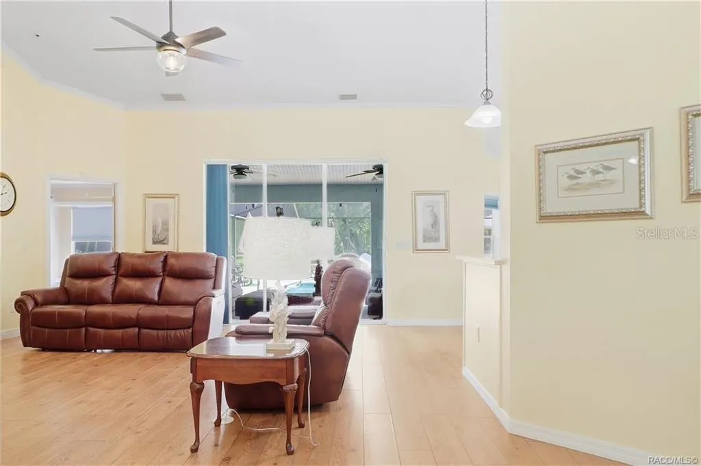 Living Room – Additional view showcasing the generous living space, vaulted ceiling, wood-look flooring &amp; access toward the pool area.