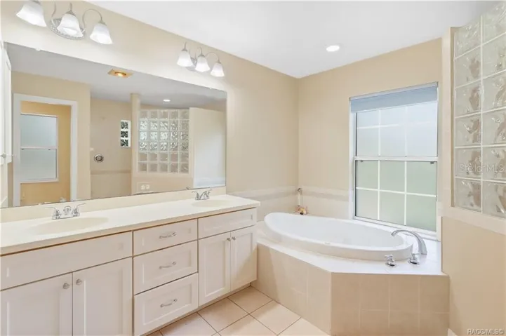Primary Bathroom – Spacious ensuite featuring a dual-sink vanity, large mirror, soaking jetted tub and tile flooring.