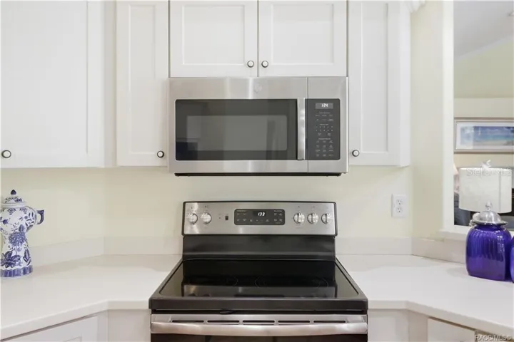 Kitchen Appliances – NEWER Stainless-steel electric range &amp; built-in microwave surrounded by white cabinetry and corian countertops.