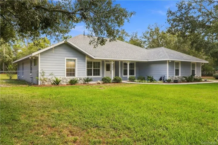 Front Exterior – BRAND NEW ROOF 2026 – Attractive front view featuring a covered front porch, mature landscaping, stone accents sitting on a fully fenced 1.25 acres.