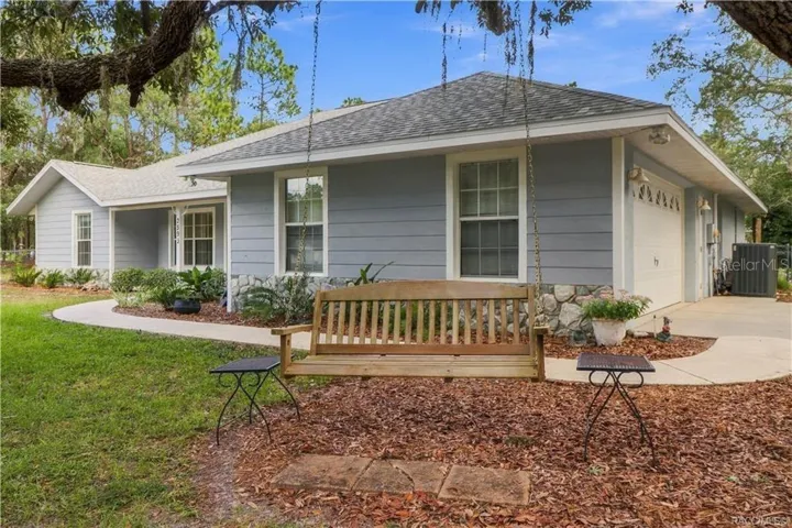 Front/Side Exterior – BRAND NEW ROOF 2026 – Side perspective showcasing the home's extended covered front porch, stone accents, mature landscaping. (Swing does not convey).