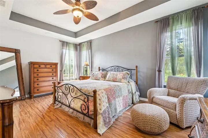 18'6" x 13' Primary Bedroom w/ engineered wood flooring, tray ceiling, ceiling fan &amp; a private conservation area view