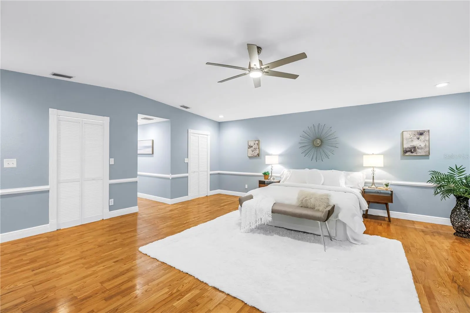 Exquisite primary bedroom suite featuring dual expansive walk-in closets, vaulted ceilings, a dedicated sitting area, hardwood flooring, and a private en suite bathroom.