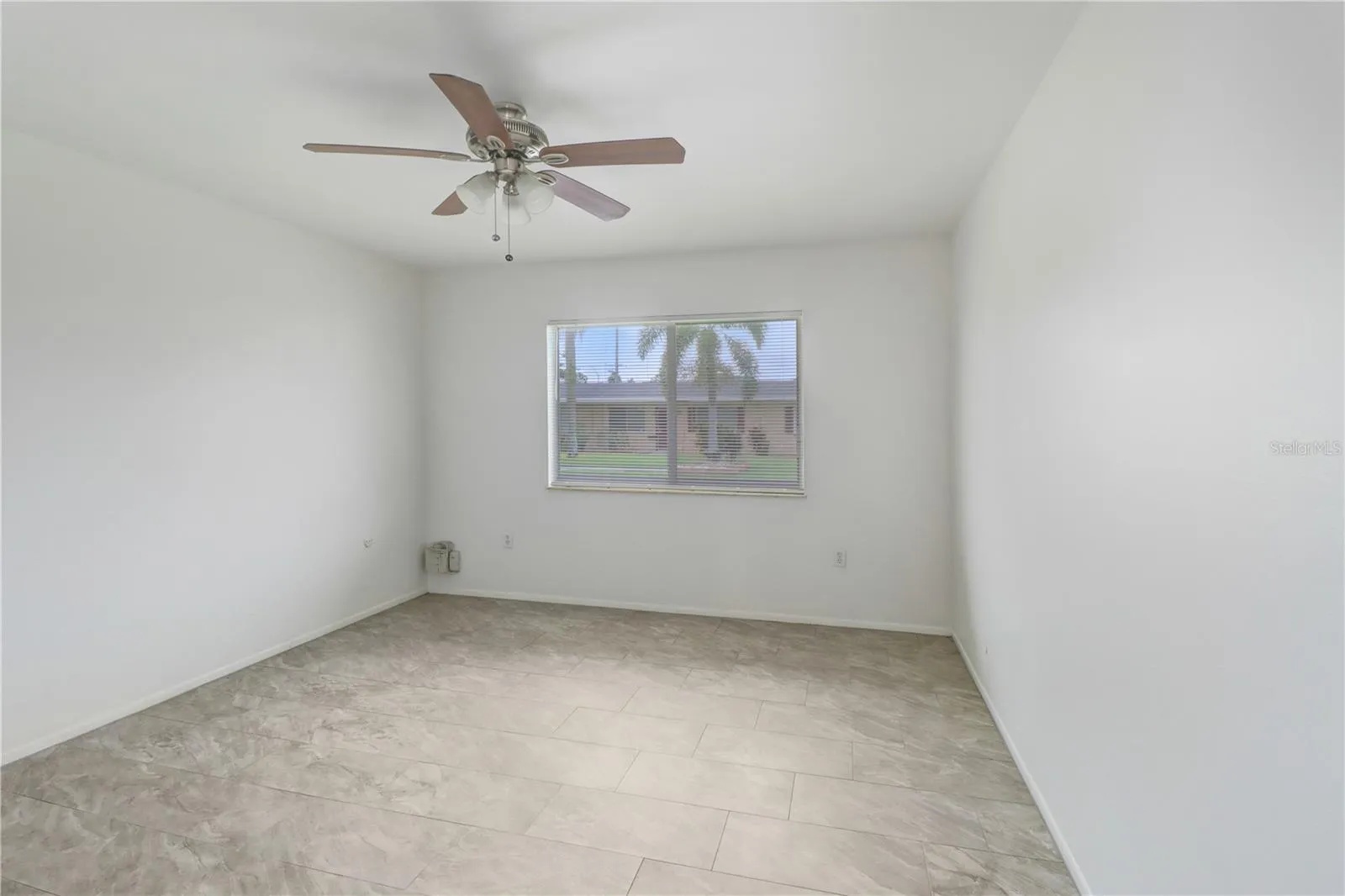 The primary bedroom features tile flooring, a ceiling fan, and a large window that provides an abundance of natural light.