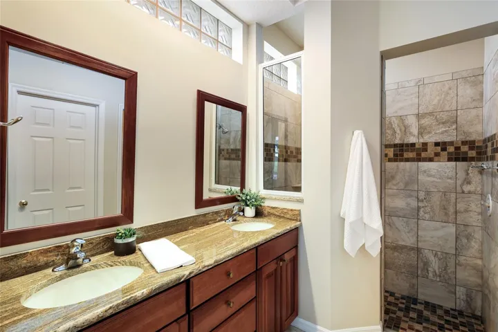 Ensuite bathroom with dual sink vanity, walk-in tile shower, private water closet and sizable walk-in closet