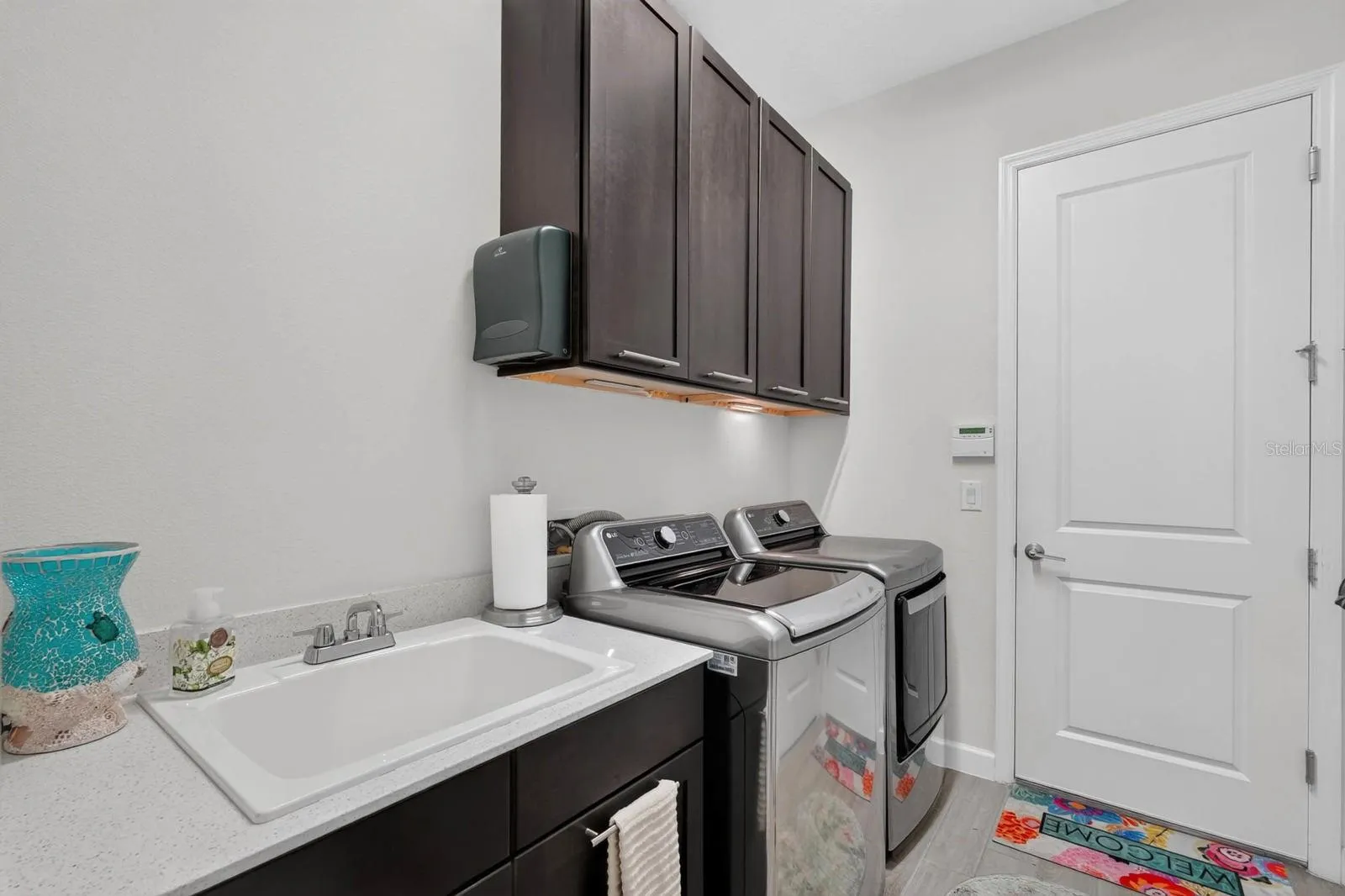 Laundry room has sink with cabinet plus overhead cabinetry and a storage closet