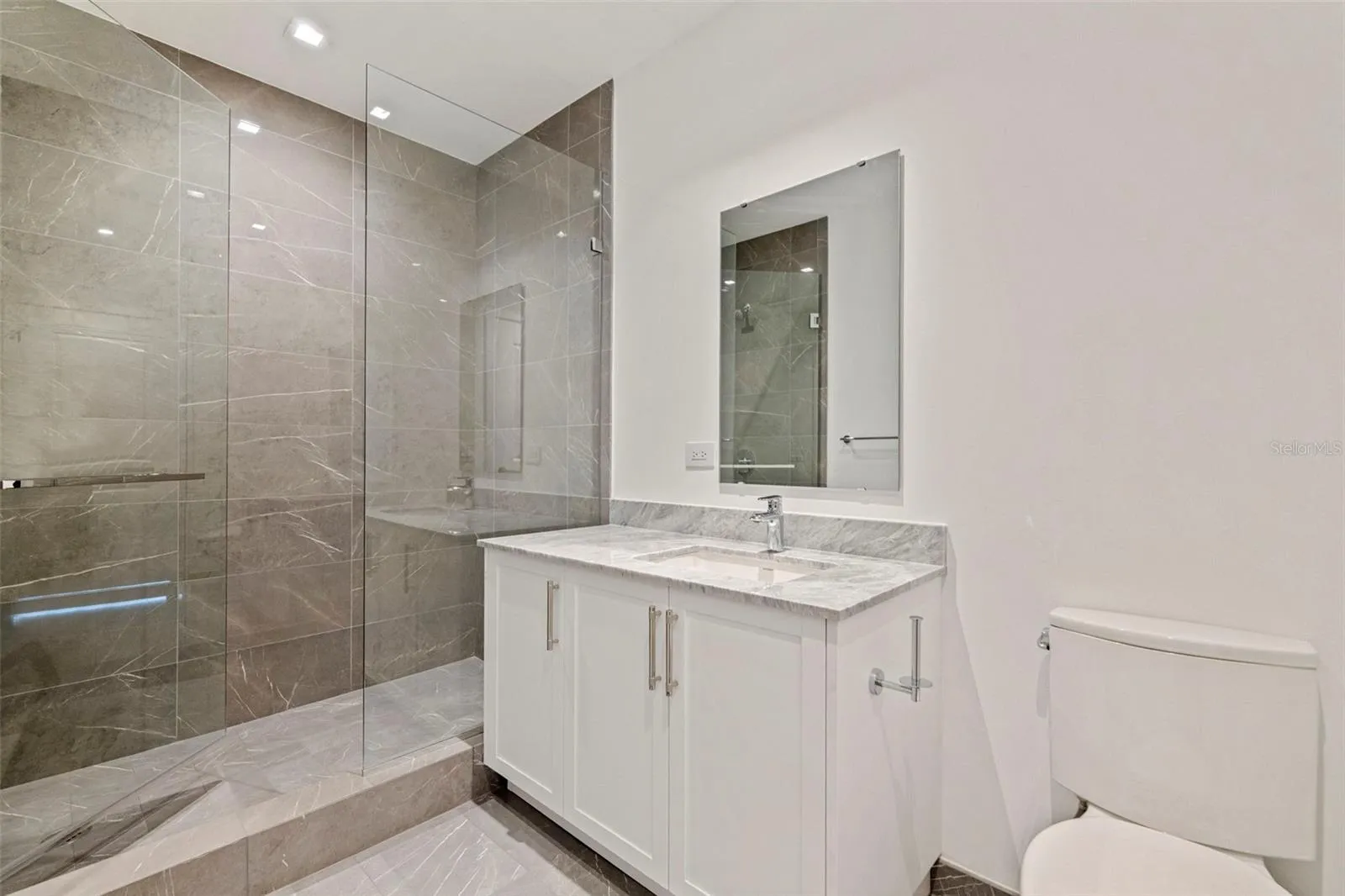 Clean-lined en-suite luxury with marble finishes and a glass-enclosed shower.