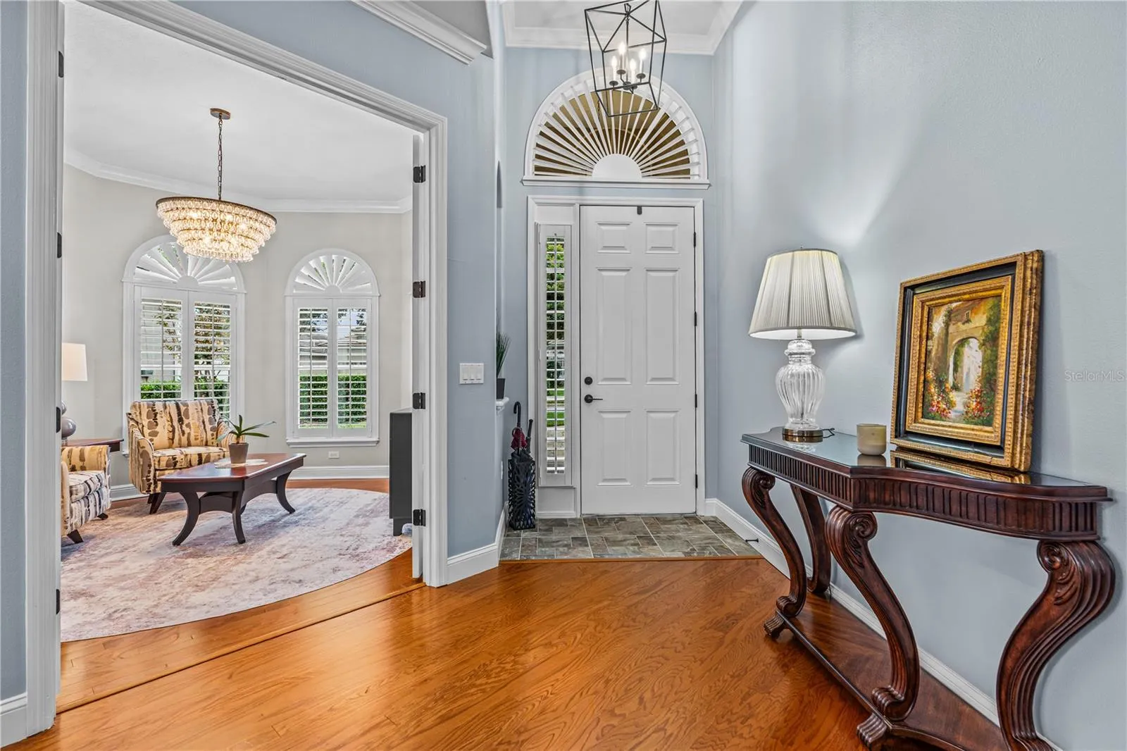 In the foyer looking toward the front door with the pretty arched transom window and into the front den/office through the open French doors
