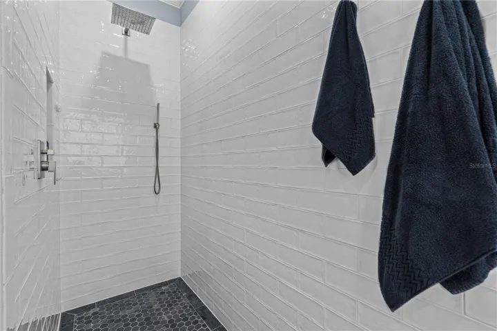 Walk-in/roll-in (no threshold) shower with rain shower head and spray wand; A storage niche is tucked away on the left