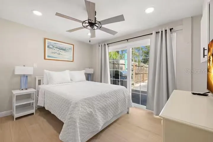 Light-filled primary bedroom with LVP flooring, ceiling fan, and sliding glass doors providing direct access to the pool and backyard.