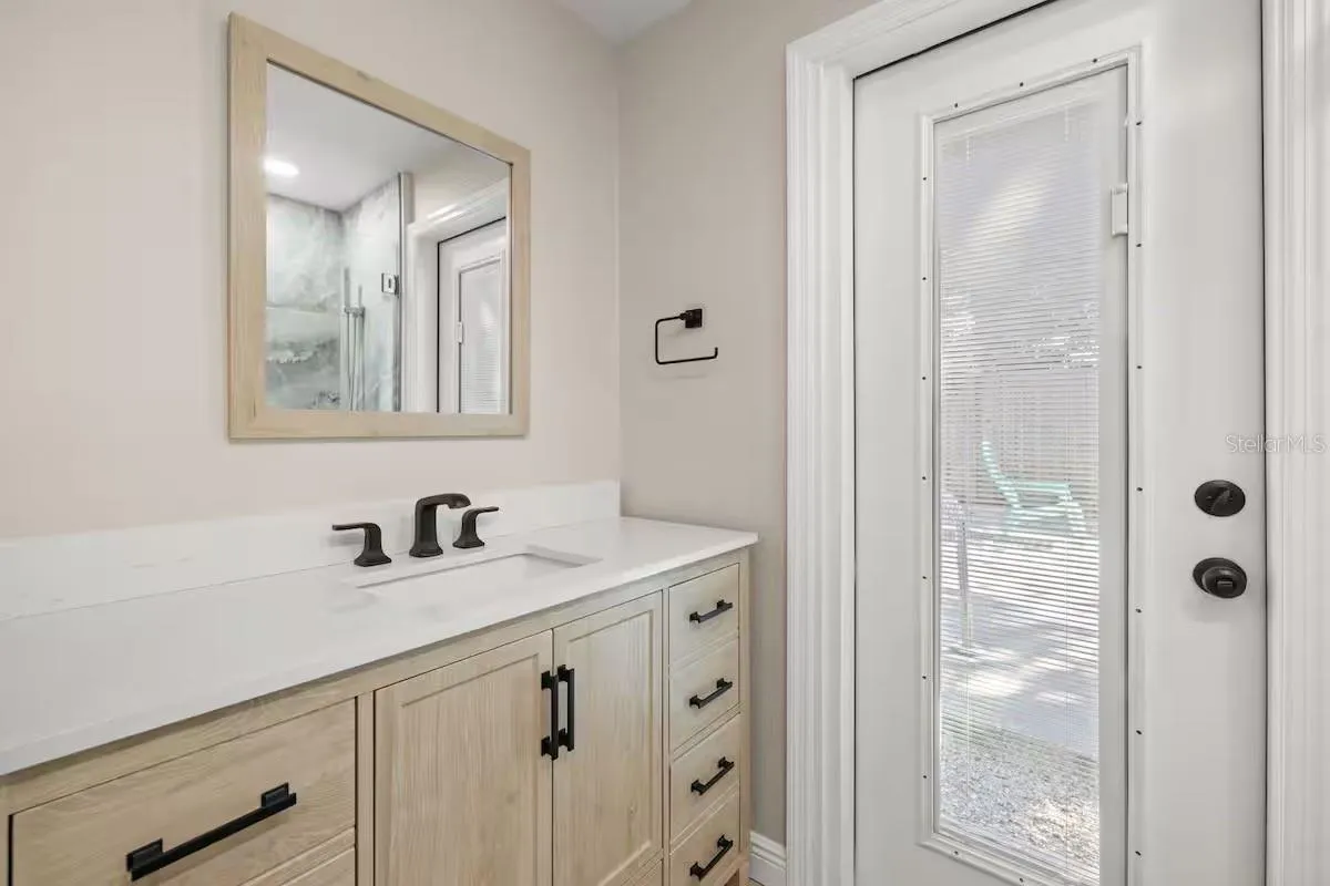 Updated vanity with solid-surface countertop, modern black fixtures, and a private exterior door offering convenient access to the pool area.