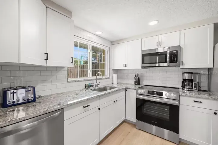 Crisp white cabinetry, stainless steel appliances, granite counters, and subway tile create a bright, fresh kitchen with plenty of workspace and storage.