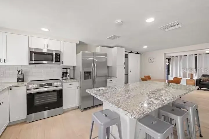 Renovated kitchen features white shaker-style cabinetry, granite countertops, stainless steel appliances, subway tile backsplash, and an oversized island with seating.