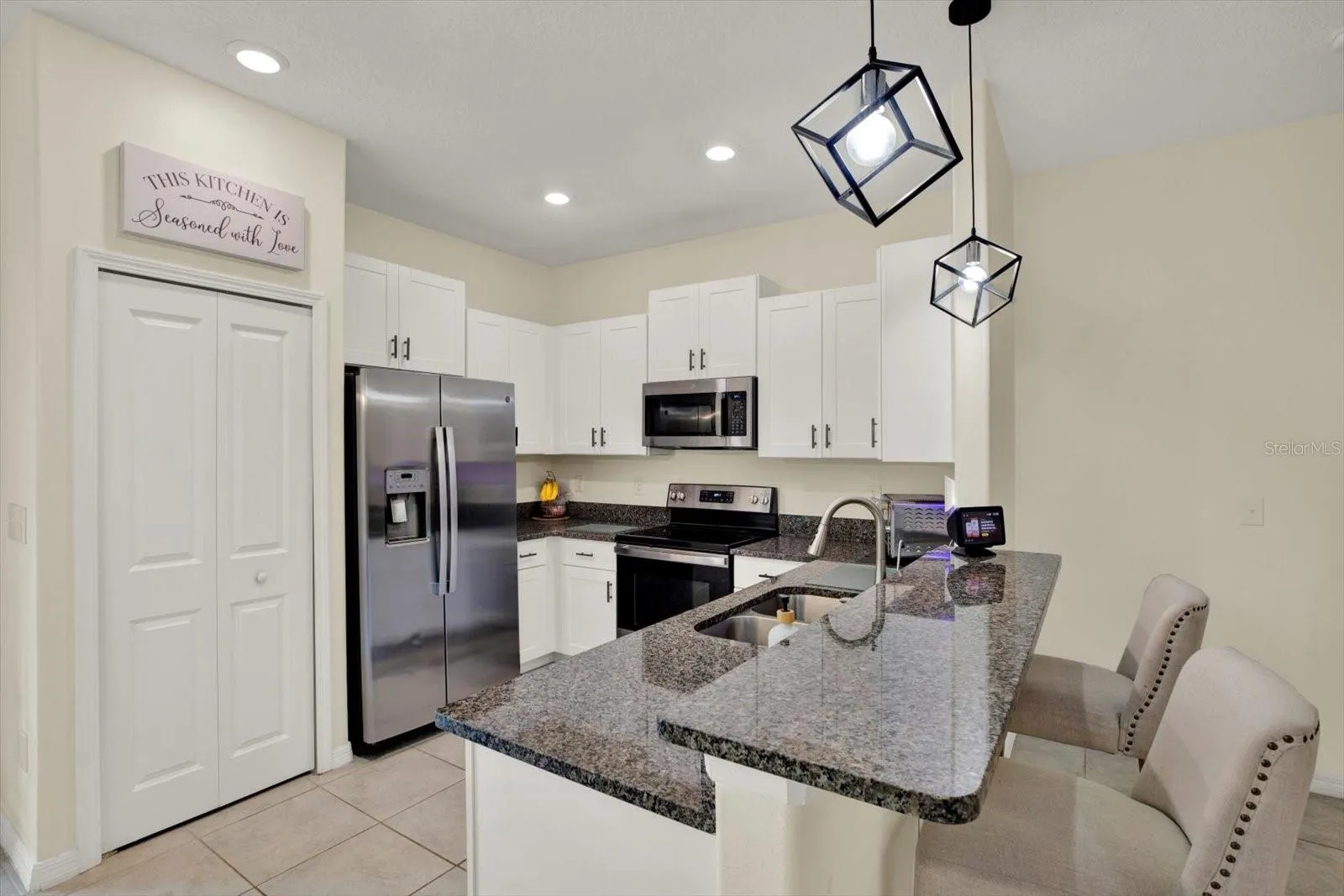 Kitchen with white cabinets, pantry, granite counters, counter seating, and stainless appliances