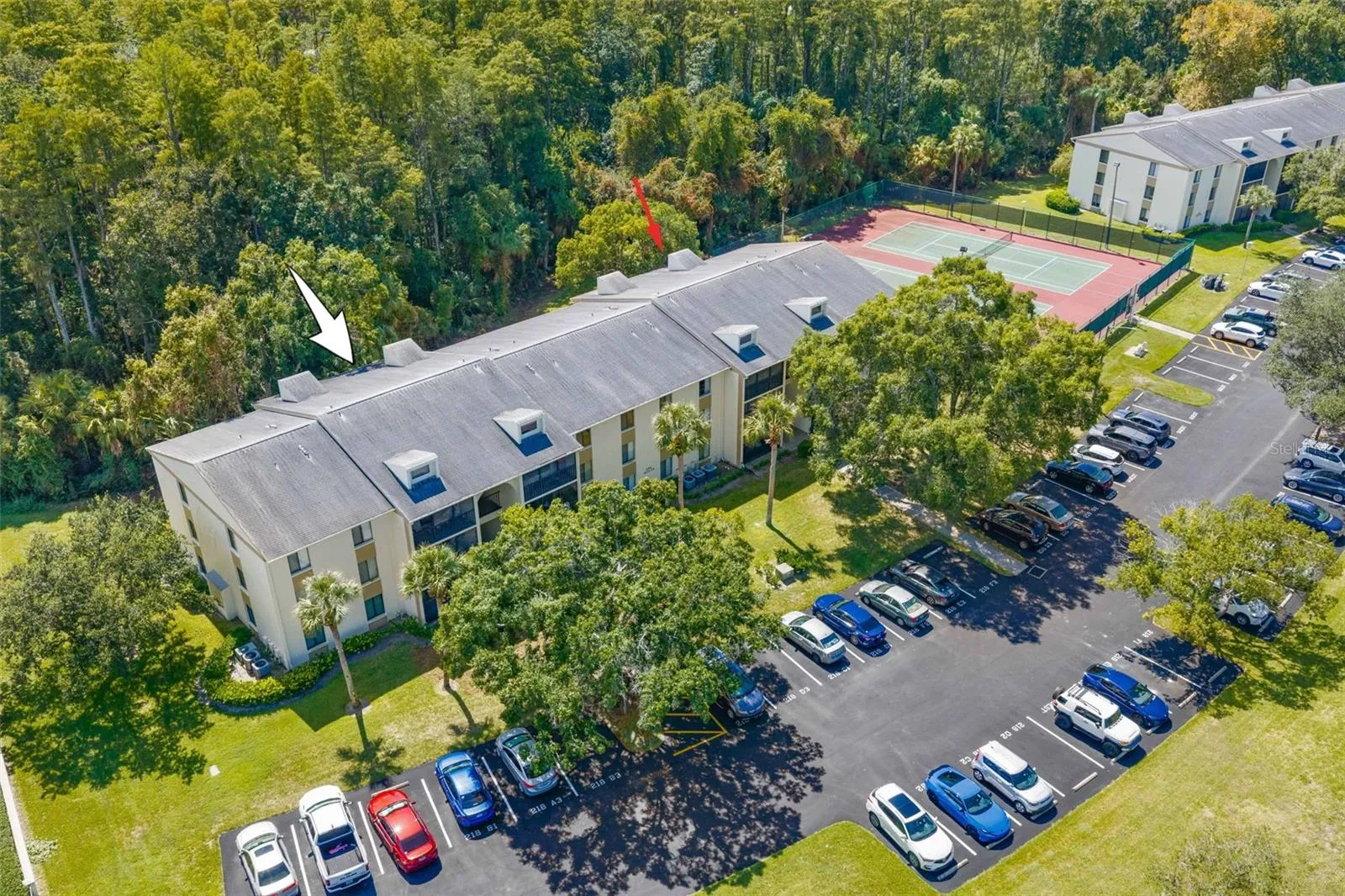 The arrow marks Unit F1’s first-floor location, with Brooker Creek Preserve directly behind the building, tennis courts just steps away, and parking conveniently located out front.