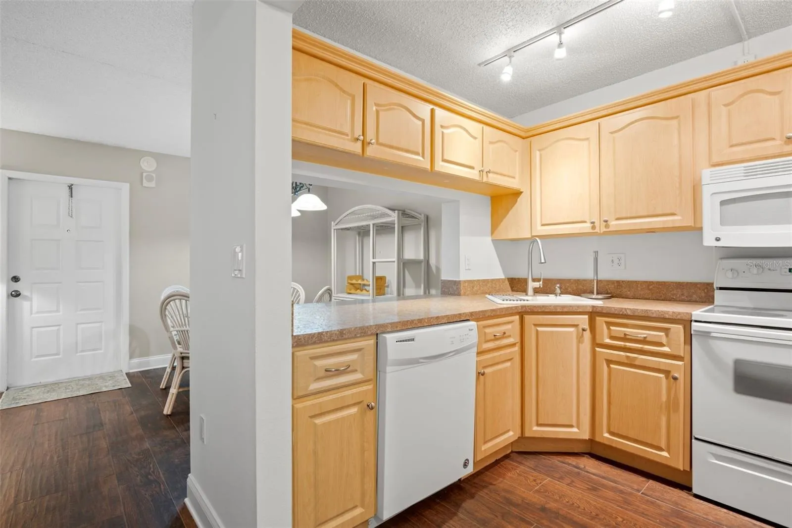 The kitchen wraps around the corner with plentiful cabinetry and counter space, a corner sink, track lighting, and an open pass-through that keeps it connected to the dining area.