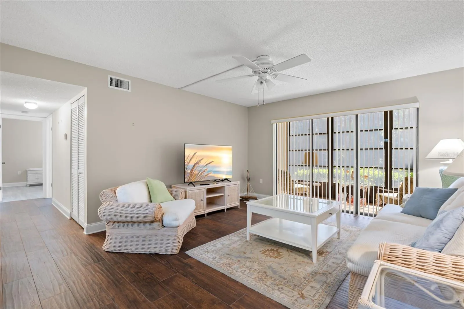 The living room features 2021 wood-look tile flooring, a ceiling fan, and wide sliding glass doors that open to the screened lanai and preserve view beyond.