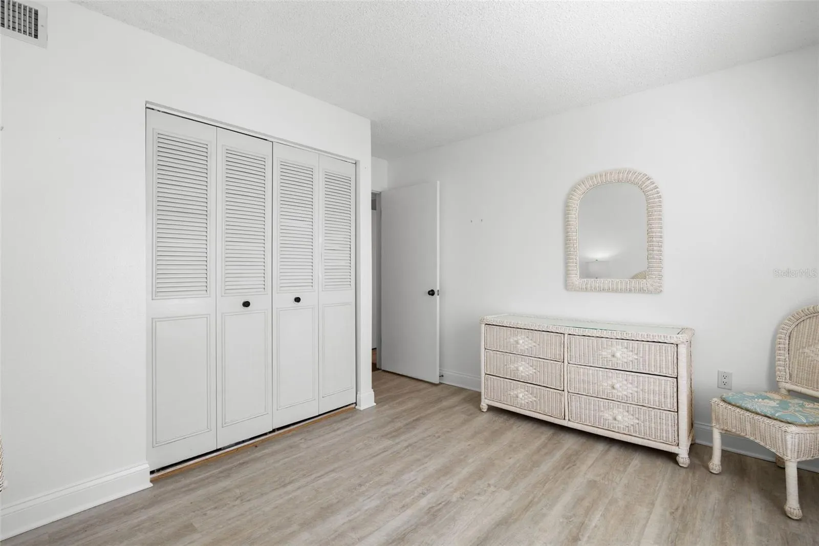 Louvered closet doors gives the second bedroom plenty of built-in storage, while the light flooring and neutral walls keep the room feeling open and flexible.