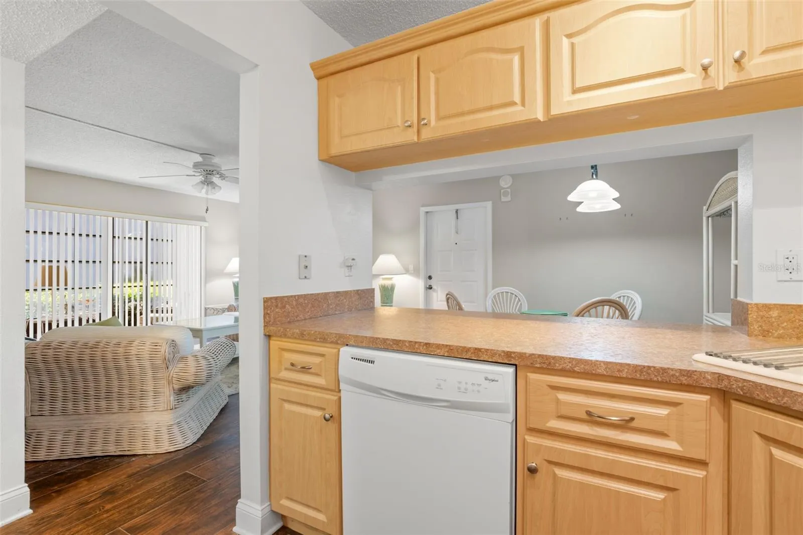 The kitchen’s wide pass-through doubles as a breakfast bar, with warm wood cabinetry, generous counter space, and a dishwasher positioned conveniently beneath.