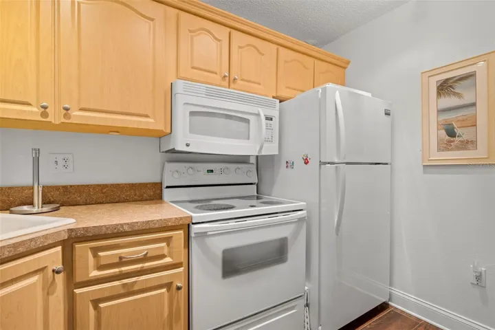 White appliances keep the kitchen bright and cohesive, with an electric range, built-in microwave, and full-size refrigerator framed by abundant upper cabinetry.