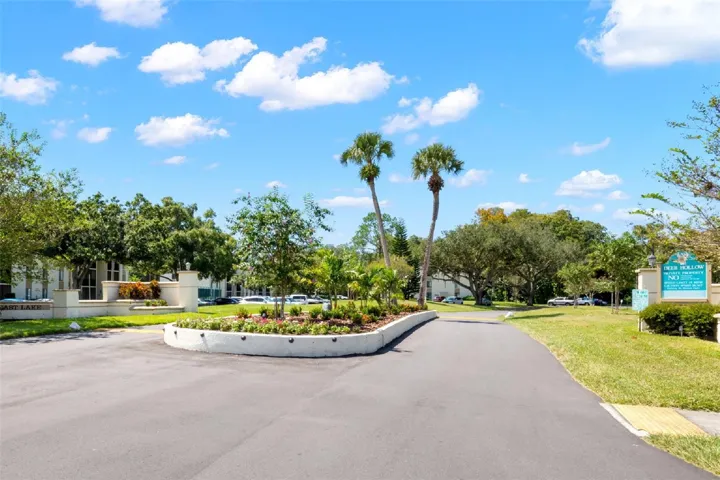 A landscaped entrance with palms, flowering beds, and mature trees sets the tone for the community’s established, well-kept surroundings.