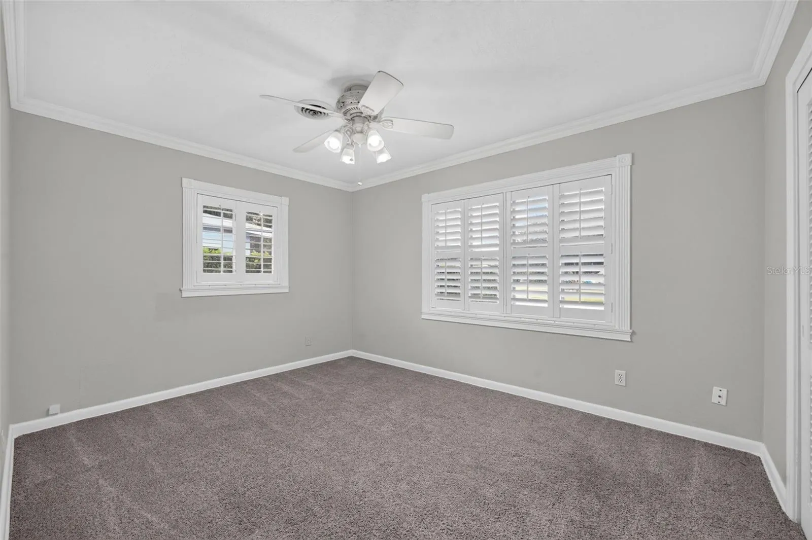 Primary Bedroom — Ample-sized primary bedroom positioned at the rear of the home with neutral carpeting, crown molding and custom interior shutters.