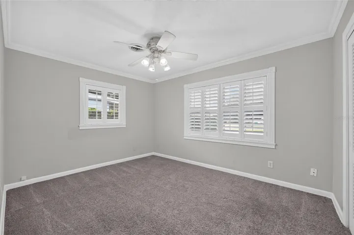 Primary Bedroom — Ample-sized primary bedroom positioned at the rear of the home with neutral carpeting, crown molding and custom interior shutters.