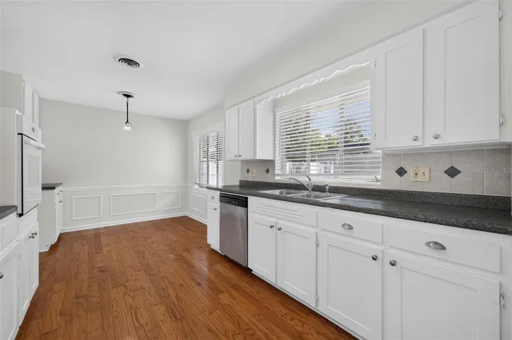 Kitchen — Charming kitchen retaining its original real-wood cabinetry, with a built-in oven, glass cooktop, stainless-steel dishwasher and hardwood flooring.