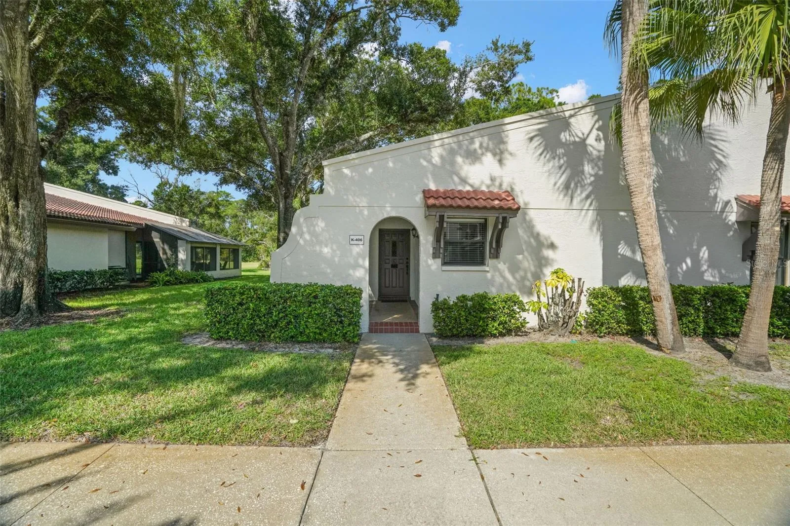 A recessed arched entry creates a sheltered welcome, with no stairs between the sidewalk and front door. Mature landscaping, palms, and tile accents give the first-floor end unit a little architectural character while keeping the approach simple and easy.