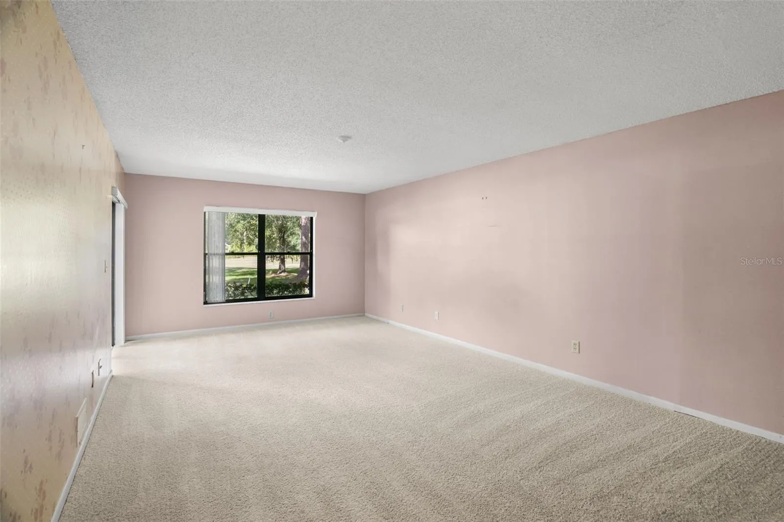 The oversized primary bedroom offers exceptional flexibility, with plenty of room for a king-size bed, dressers, and a separate sitting or reading area. Newer carpet keeps the space comfortable underfoot, while a large window and sliding glass door bring in natural light and connect the room directly to the screened lanai.