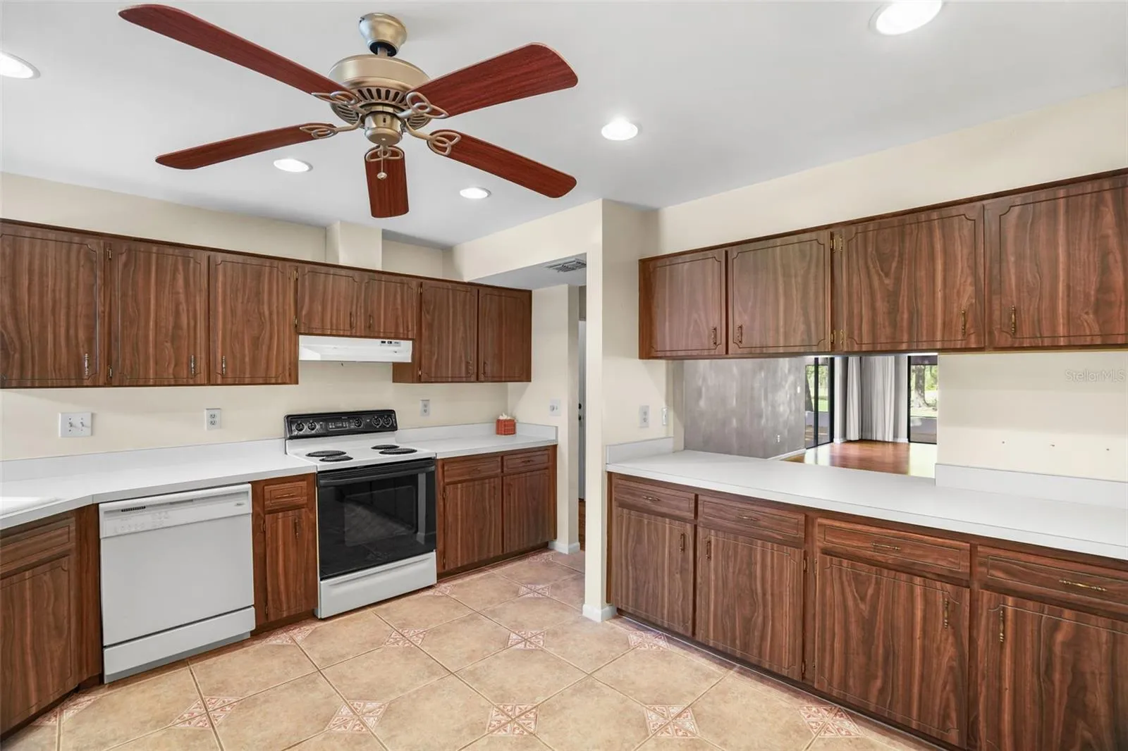 A second wall of cabinetry adds even more storage and counter space, while the wide pass-through keeps the kitchen connected to the main living area. Recessed lighting and a ceiling fan brighten the generous workspace, with enough floor area to consider a small island or movable prep table.