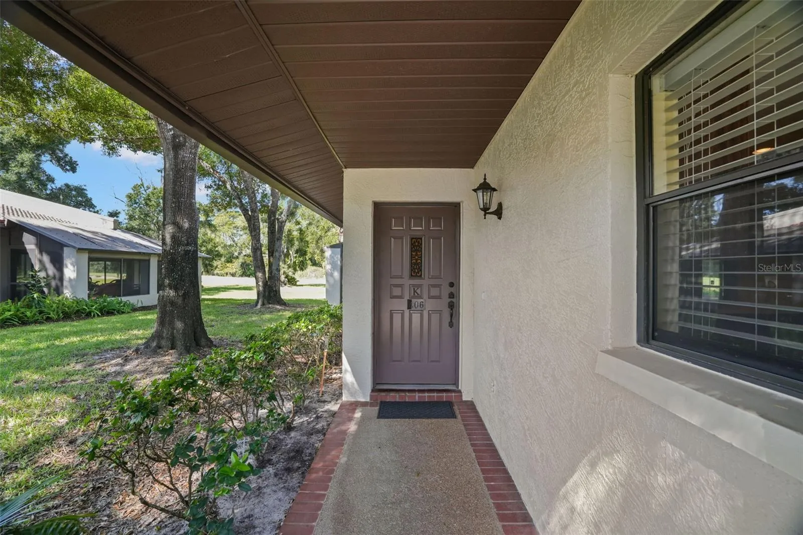 A covered walkway leads to the front door, edged in brick and shaded by mature trees. A large front window brings light into the condo, while the end-unit location keeps the entry feeling more open and tucked away from passing foot traffic.