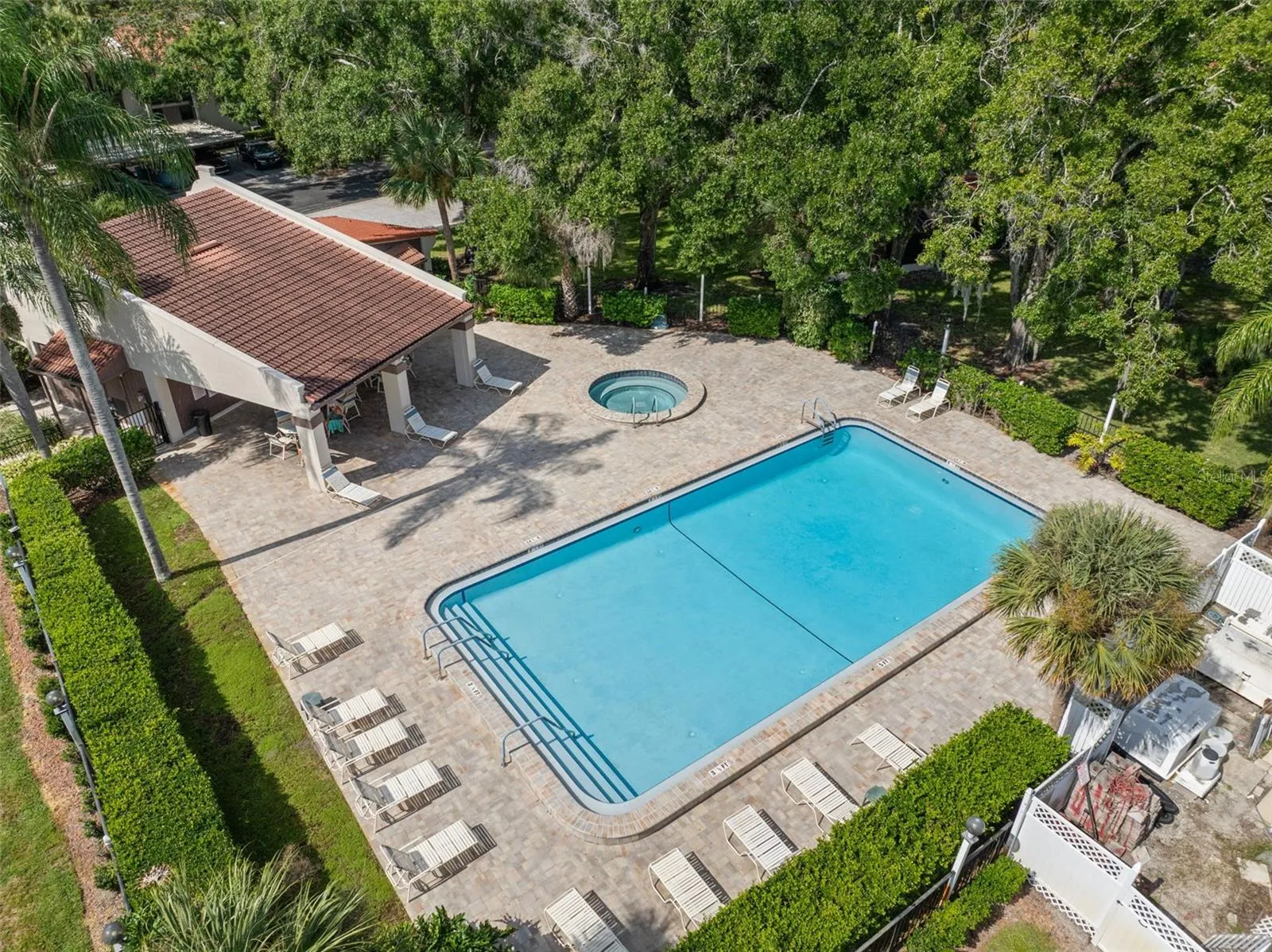 The community pool offers plenty of room to swim, lounge, and unwind, with a separate spa, shaded seating under the covered pavilion, and an expansive paver deck surrounded by mature landscaping.