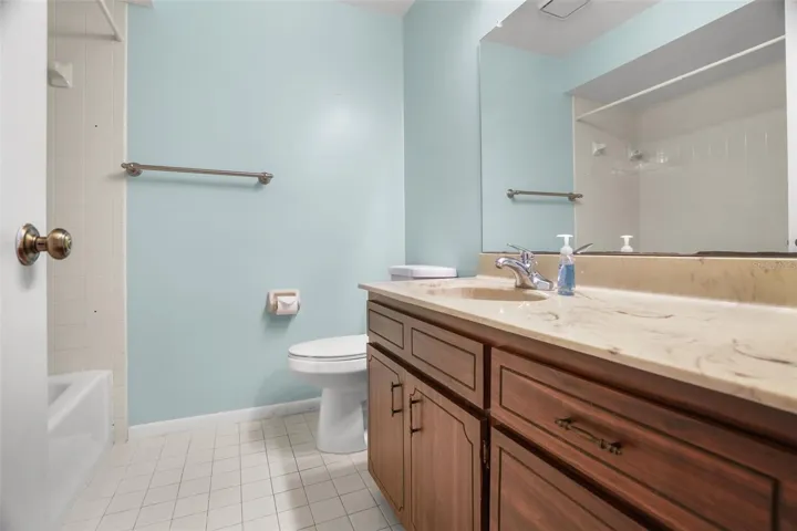 The second full bath includes a tub-and-shower combination, single-sink vanity with cabinet and drawer storage, a large wall mirror, and tiled flooring. Its straightforward layout gives guests or the second bedroom a practical, private bath of their own.