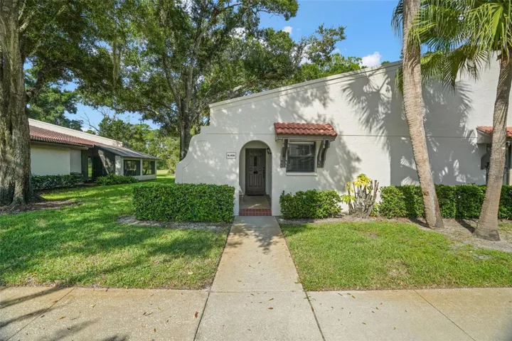 A recessed arched entry creates a sheltered welcome, with no stairs between the sidewalk and front door. Mature landscaping, palms, and tile accents give the first-floor end unit a little architectural character while keeping the approach simple and easy.