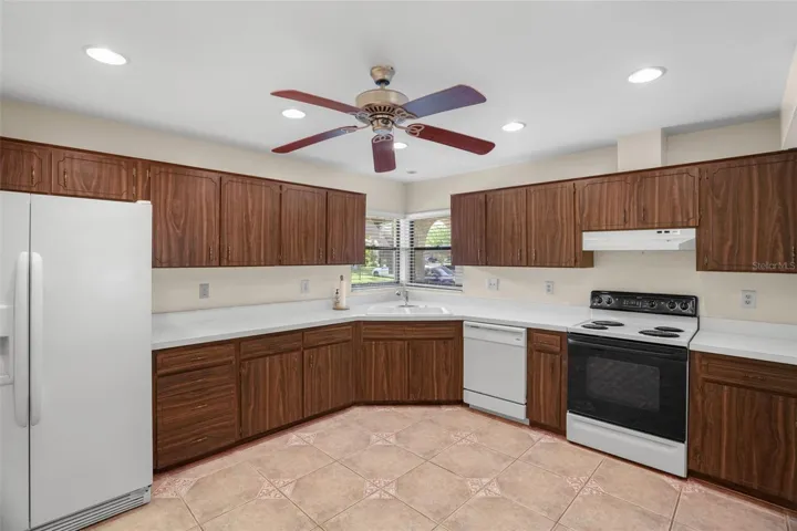 The generous U-shaped kitchen provides abundant cabinetry and counter space, a corner sink beneath two windows, recessed lighting, and enough open floor area to consider a small island or movable worktable.
