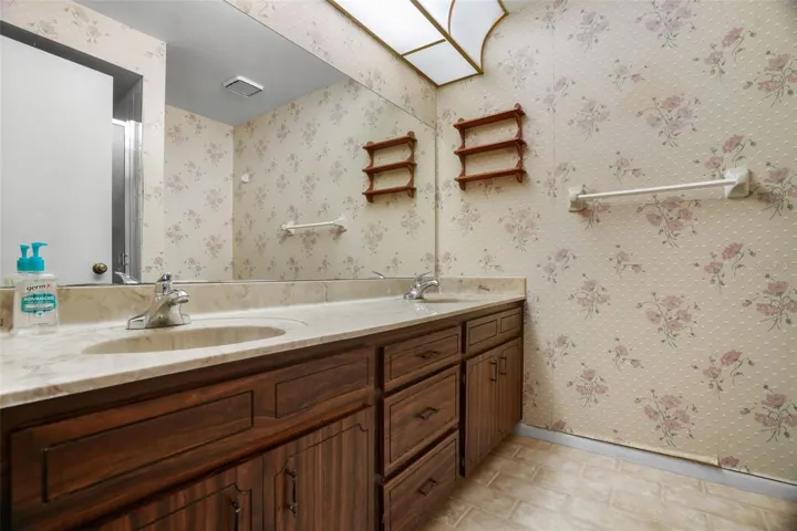 The primary bath includes a long double-sink vanity with abundant cabinet and drawer storage, a full-width mirror, and overhead lighting. The generous counter space gives two people room to get ready comfortably, with plenty of opportunity to refresh the finishes over time.