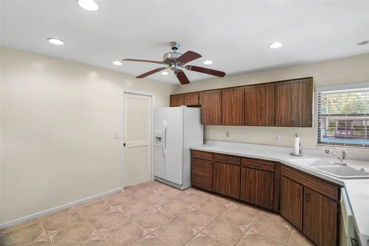 The generously sized kitchen gives you plenty to work with, including a long run of cabinetry and counter space, a double sink beneath the window, recessed lighting, a ceiling fan, and room to reimagine the layout over time. Tile flooring keeps the work area practical, while the large footprint offers flexibility for future updates.