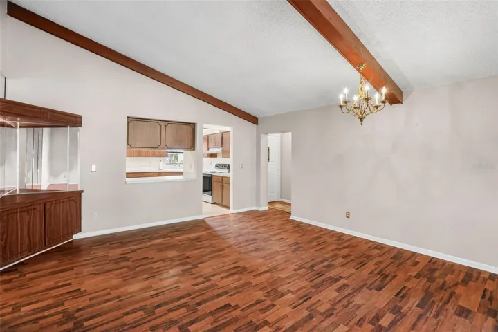A traditional chandelier defines the dining area beneath the vaulted ceiling and exposed wood beams. The pass-through to the kitchen keeps serving easy, while the generous footprint leaves plenty of room for a full-size dining table and additional furniture.