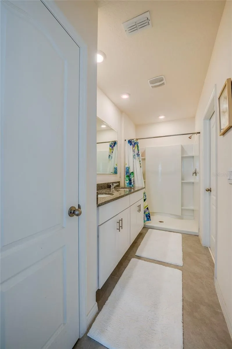 Ensuite bath features a long vanity with granite countertop, white cabinetry, a large mirror, and a walk-in shower with built-in shelving.