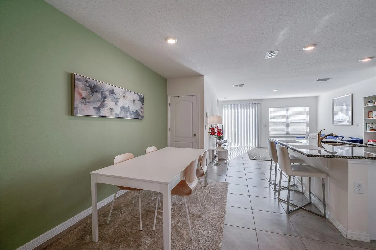 Open dining space flows seamlessly into the kitchen and living area, with recessed lighting and an accent wall adding a touch of color.