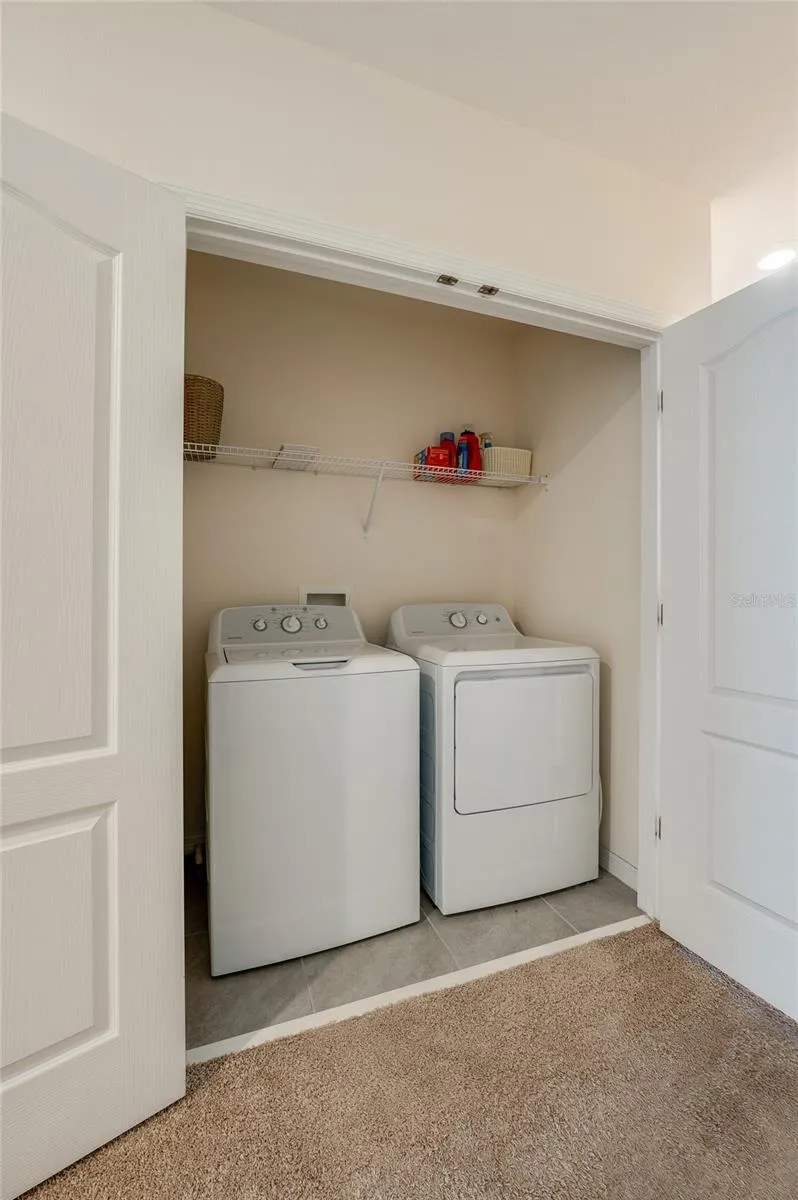 Convenient upstairs laundry closet offers side-by-side washer and dryer space with overhead shelving for supplies.