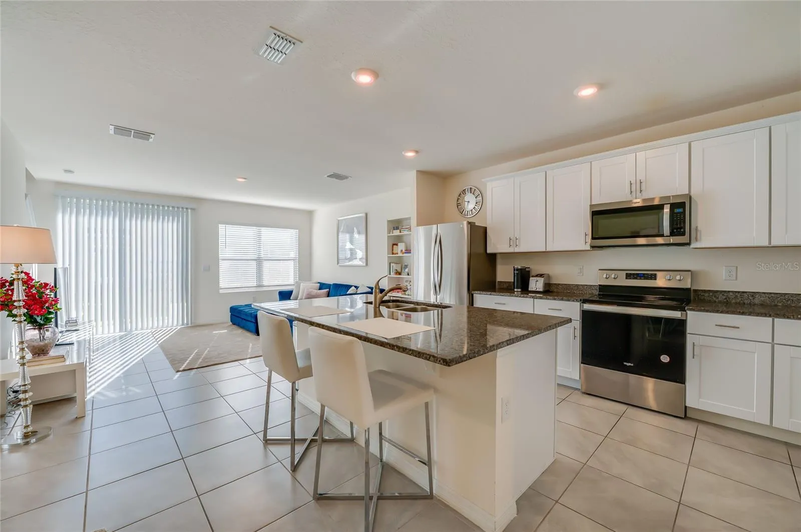 Open kitchen features white cabinetry, granite countertops, stainless steel appliances, and a generous island with breakfast-bar seating.