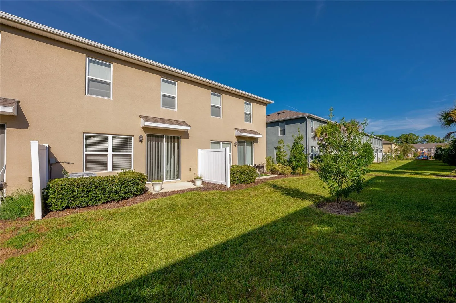 Rear exterior view highlights the patio access, landscaped green space, and open lawn extending behind the townhome.