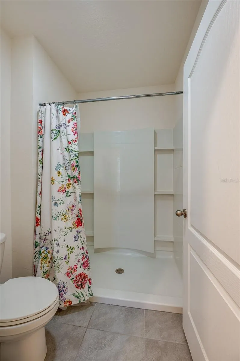 Separate bath area features a walk-in shower with built-in surround shelving and neutral tile flooring.