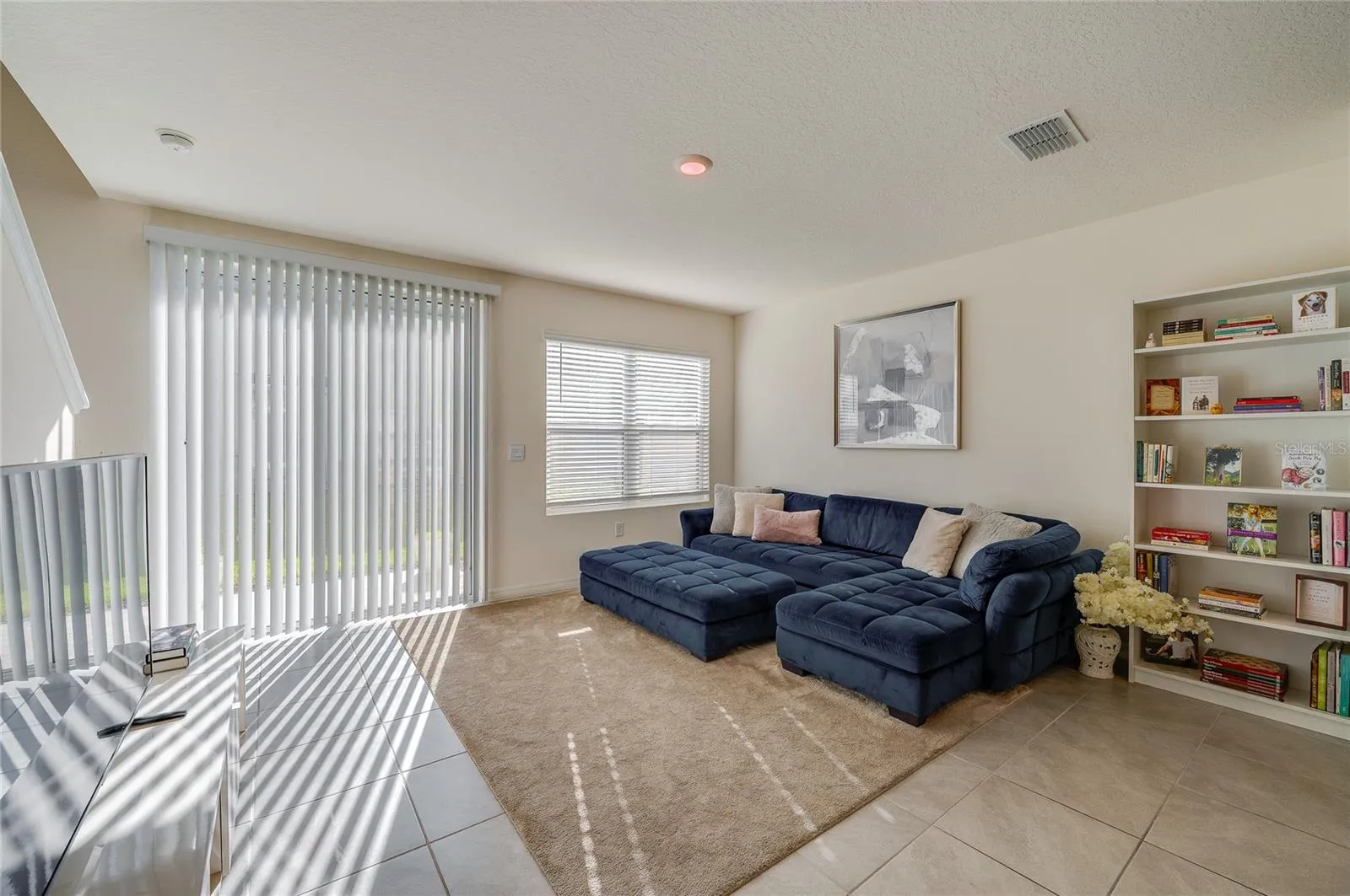 Natural light fills the living area through a large window and sliding glass doors, while built-in shelving provides convenient display and storage space