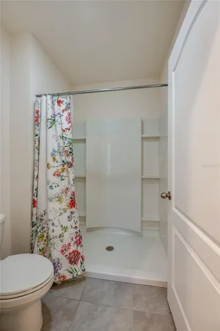 Separate bath area features a walk-in shower with built-in surround shelving and neutral tile flooring.