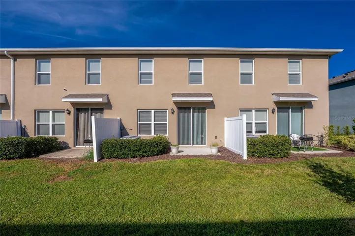 Rear view showcases the townhome’s patio area with sliding-door access, landscaped surroundings, and an open grassy area beyond.