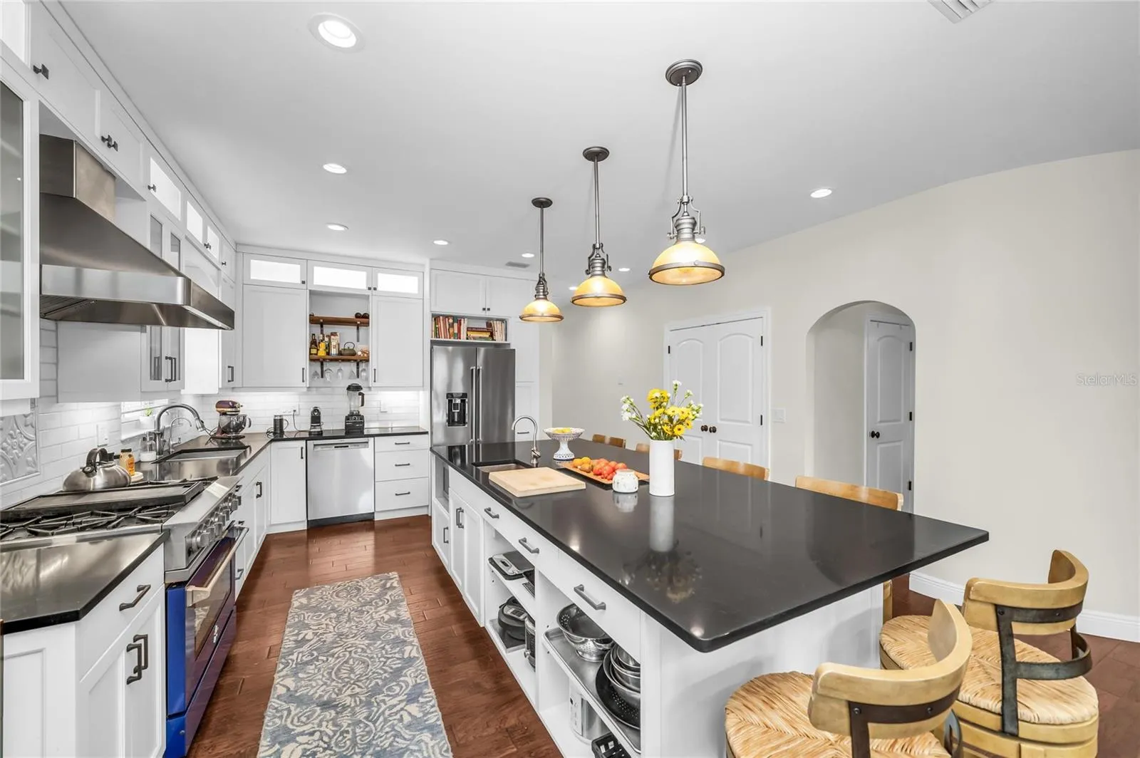 This chef-inspired kitchen is appointed with a professional gas range and hood, stainless-steel refrigerator and dishwasher, abundant cabinetry, and an oversized island with quartz countertops and built-in storage.